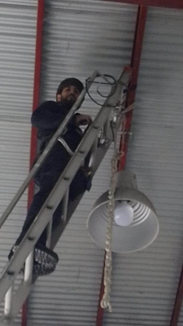 Javier subido a una escalera instalando una luminaria en un techo de chapa